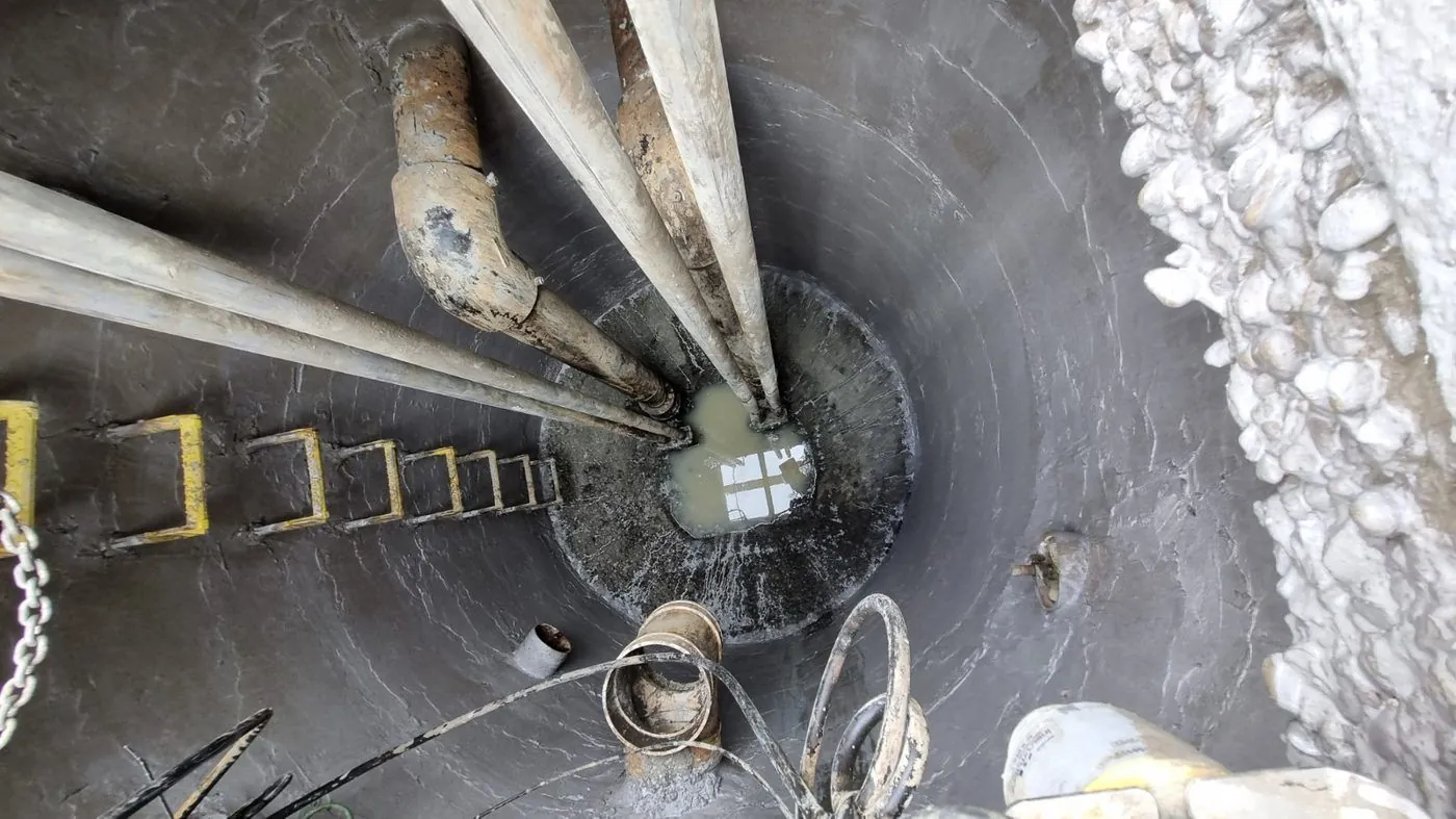 Looking down into a deep concrete chamber with pipework, access rungs and services in an operating water asset.